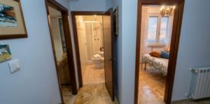 Appartamento vista mare: corridoio blu, bagno bianco a sinistra e camera da letto con lampadario.