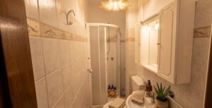 Bagno compatto appartamento vista mare con doccia in vetro, lavandino e specchio illuminato.