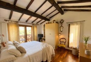 Camera in casale a Camaiore: letto bianco, travi e luce naturale per relax in Versilia.