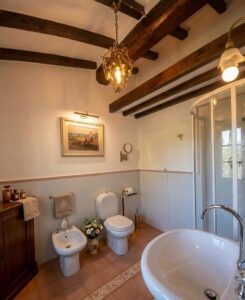 Bagno elegante in casale a Camaiore: travi legno, due toilet e doccia vetro in Versilia.