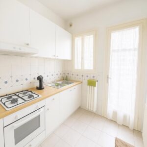 Cucina L-shape bianca e legno con finestra a vetri e accessori scuri.