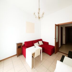 Soggiorno moderno con sofà L-rosso e tavoli bianchi, stile villa pisana minimalista.