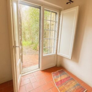 Porta e finestra bianche su giardino verde, villa pisana rustica, con vista boscosa.
