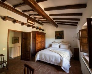 Camera rustica a Camaiore: letto bianco, travi in legno e mobili scuri, ideale in casale o villa.