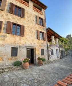 Casale rustico a Camaiore in Versilia con pietra, vialetto e pergola, vista mare e cielo blu.
