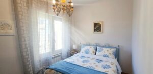 Camera bianca e blu con letto fiorato e vista mare, ideale per appartamento vista mare.