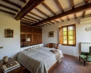 Camera bianca in villa vista mare Versilia a Camaiore con travi, finestra e poltrona verde.