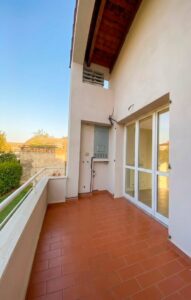 Balcone al tramonto con ringhiera bianca, porta scorrevole e vista serena su cielo blu in Italia.