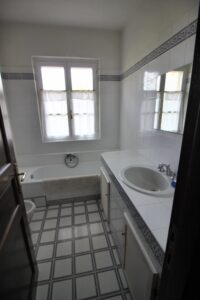 Bagno bianco con vasca centrale, lavandino, specchio e finestra.