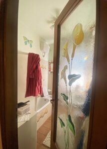 Porta vetrata floreale e bagno illuminato con tocco rosso e dragoncello.