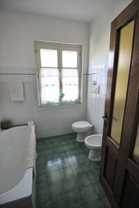Bagno luminoso con vasca bianca, wc e bidet vicino a finestra soleggiata e piastrelle verdi.
