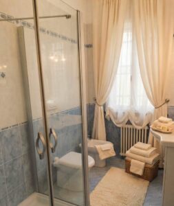 Bagno con doccia vetrata e tende azzurre mediterranee.
