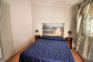 Camera compatta in villa storica con letto blu, parco e piscina panoramica dominante.