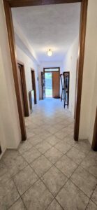 Corridoio luminoso con pavimento in ceramica e porta in legno aperta.