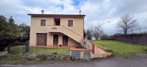 Casa di campagna con tetto in cotto, scala esterna e giardino recintato.