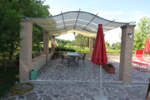 Patio coperto in giardino con tavolo da pranzo, sedie e ombrellone rosso