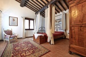 Accogliente camera da letto in prestigioso casale con terracotta, letto a colonne e armadio in legno.