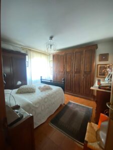 Accogliente camera da letto con letto bianco, finestra luminosa, tappeto scuro e armadi in legno.