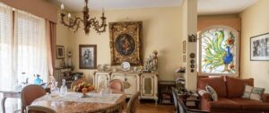 Soggiorno e sala da pranzo accoglienti con tavolo marmo, lampadario e vetrata artistica di pavone.