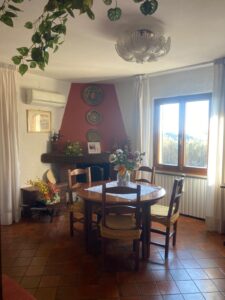 Accogliente sala da pranzo con tavolo rotondo, parete rossa, lampadario e finestra luminosa.