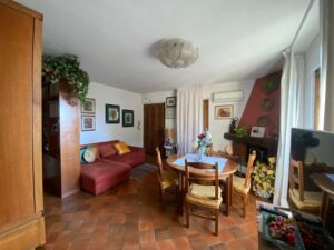Soggiorno accogliente con divano rosso, camino, tavolo rotondo e mattonelle in terracotta.