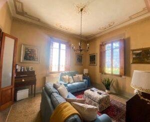 Soggiorno accogliente con divani blu, pareti beige, finestre e legno per atmosfera calda e rilassante.