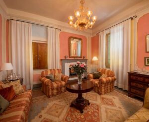 Soggiorno pesca elegante con camino, lampadario dorato, divano, poltrone e tappeto beige accogliente.