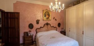 Camera da letto rosa con testiera in legno, lampadario e quadro dorato: relax elegante e tranquillo.