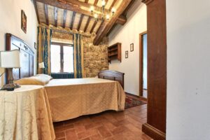 Accogliente camera da letto in prestigioso casale rustico con travi a vista e letto in legno.