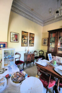 Salotto eclettico con soffitti alti, librerie antiche, vetrine e tappeto rosso.