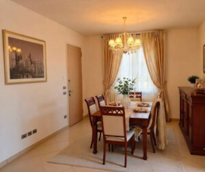Camera da pranzo classica con tavolo woodeno, sedie scure e beige, centro tavola verde, soffuso aanluento golden.