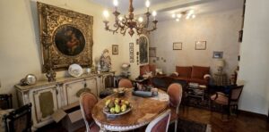 Accogliente sala da pranzo con tavolo marmo, sedie arancio e lampadario cristallo su pareti crema.