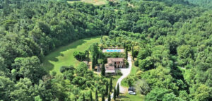 Vista aerea di prestigioso casale nel bosco con piscina e parco curato.