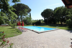 Piscina panoramica in villa di campagna, con lettini e ombrelloni rossi immersi nel verde