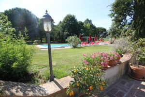 Piscina in giardino con patio fiorito, lettini e ombrelloni rossi