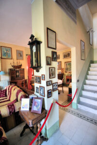 Interno di casa museo con scala in pietra, quadri e orologio a pendolo