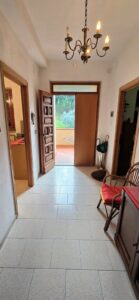 Ingresso casa luminoso con lampadario antico, porta in legno e pavimento piastrellato.