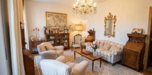 Sala vintage con chandelier di cristallo e sofà floreale, illuminata da luce naturale.