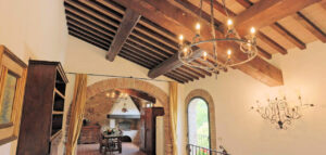 Sala luminosa di prestigioso casale con lampadario, travi in legno e arco verso la zona pranzo.