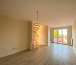 Sala vuota minimal con scala in legno e porte vetrate su giardino luminoso.