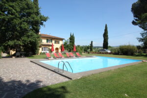 Piscina mediterranea con lettini rossi, prato verde e alberi