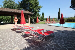 Piscina all’aperto con lettini e ombrelloni rossi su terrazza in pietra stile mediterraneo