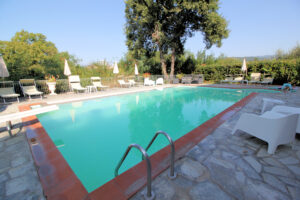 Piscina panoramica nel parco di villa storica con lettini e vista dominante.