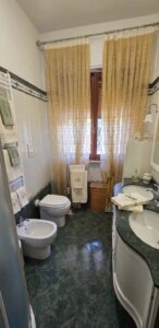 Bagno compatto dallalto: wc, lavabo, pavimento verde e finestra con luce naturale.