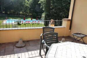 Patio con tavolo e sedie nere, vista piscina blu e giardino alberato.