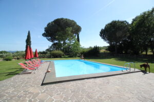 Piscina in giardino con lettini rossi, ombrelloni e patio in pietra