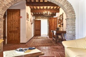 Accogliente interno del prestigioso casale in mattoni e legno con divano crema e corridoio illuminato.