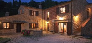 Prestigioso casale in pietra di notte con luci calde e giardino, accoglienza serena e tranquilla.