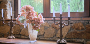 Vaso rosa e candelabri su tavolo in legno in un prestigioso casale con muro in pietra.