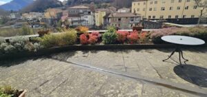 Terrazza fiorita sulle mura di Castelnuovo Garfagnana con vista paese montano e appartamento ristrutturato.